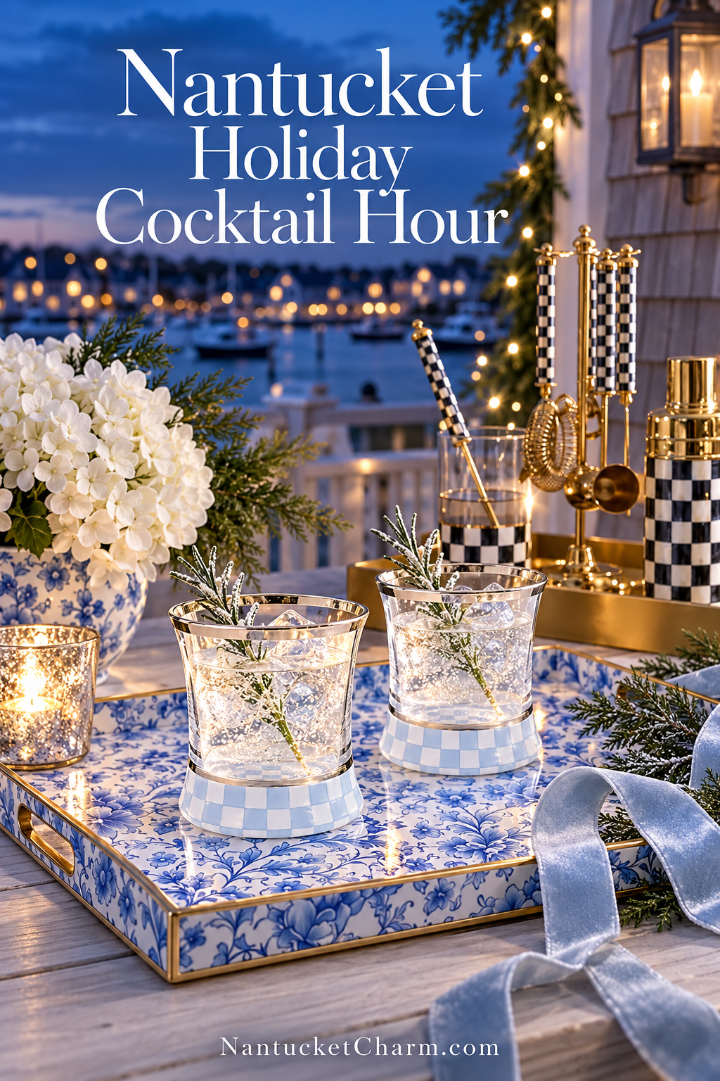 Two silver-rimmed cocktails with frosted rosemary on a blue-and-white floral tray, MacKenzie-Childs check barware, white hydrangeas in a chinoiserie vase, mercury glass candle and ice blue velvet ribbon overlooking Nantucket harbor at dusk.